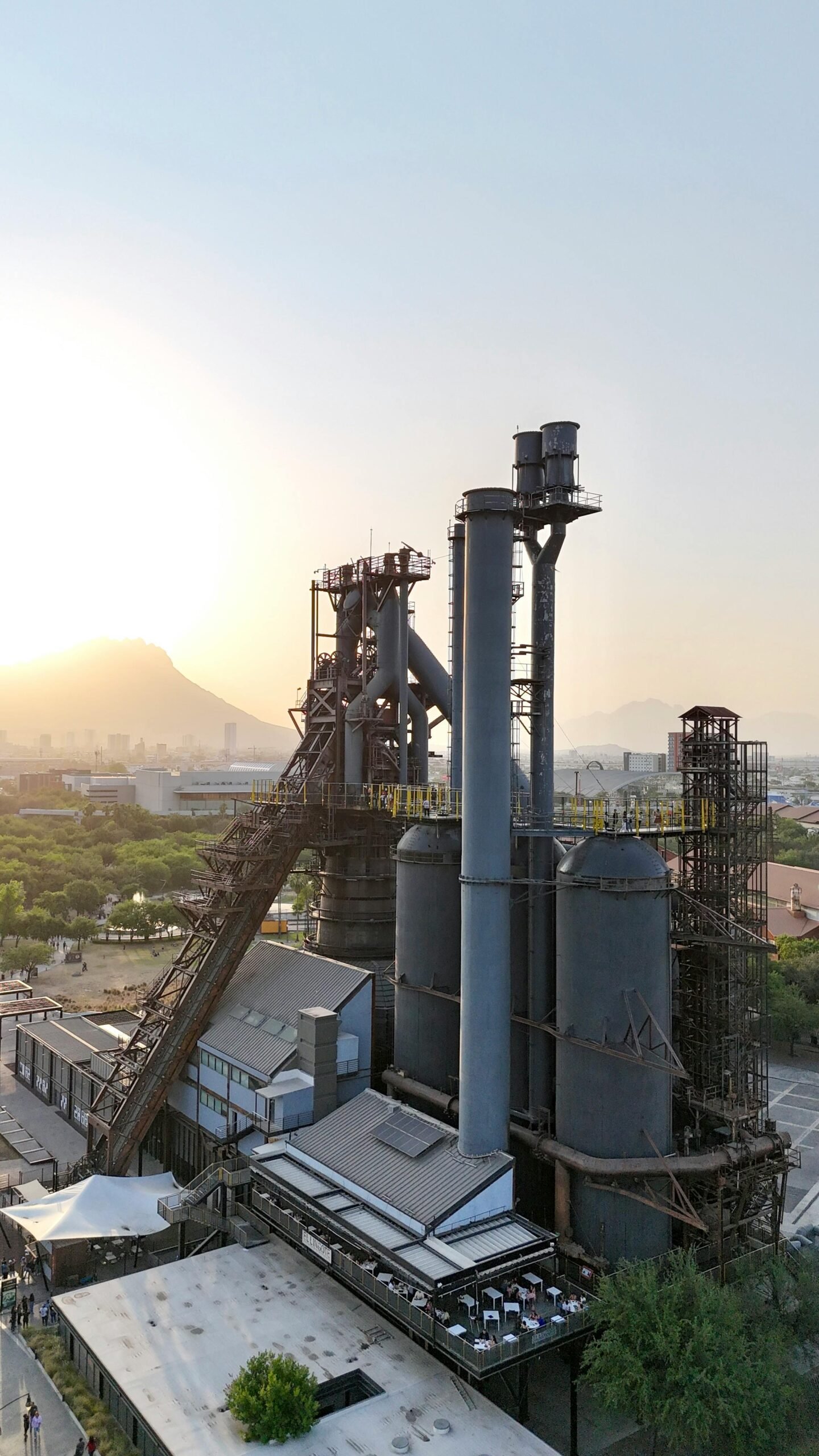 Aerial view of a steel plant at sunset with mountains in the backdrop.